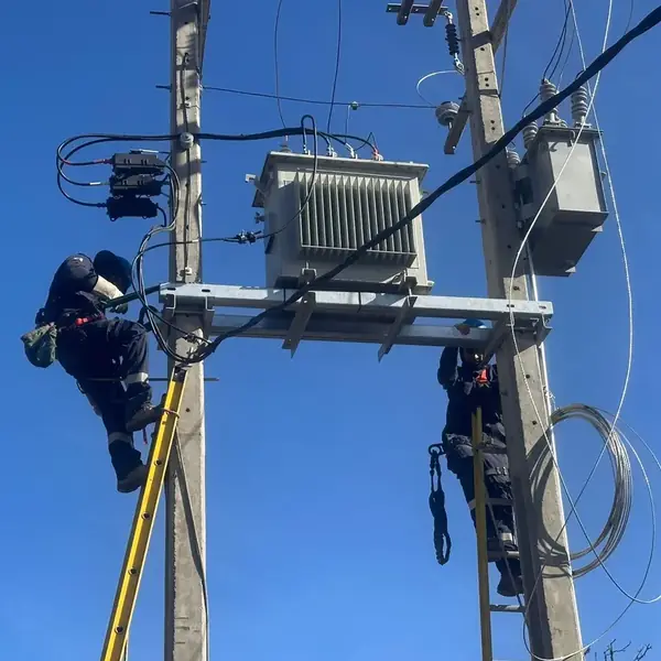 Dos técnicos con arnés montando un transformador de distribución sobre estructura